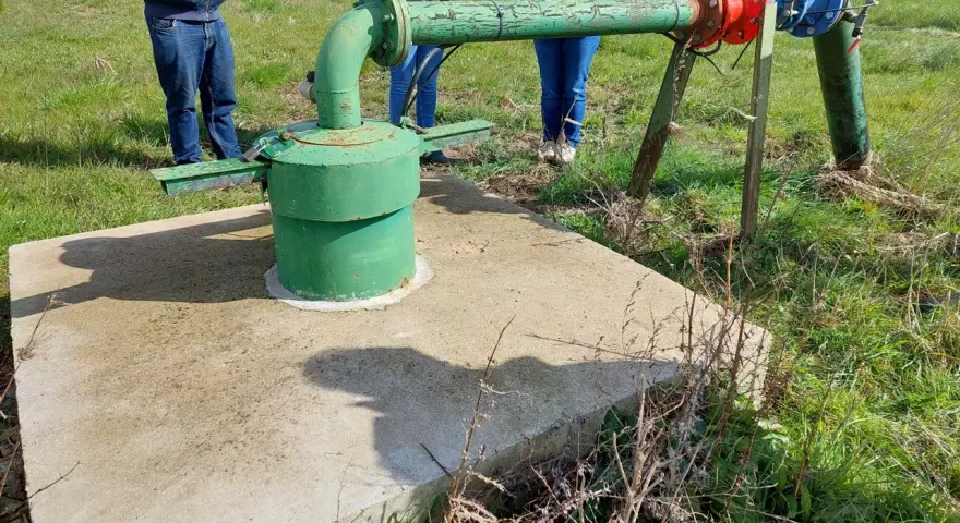 Installation de forage agricole, respectant la réglementation. Des personnes observent le système de pompage et de tuyauterie verte et bleue.