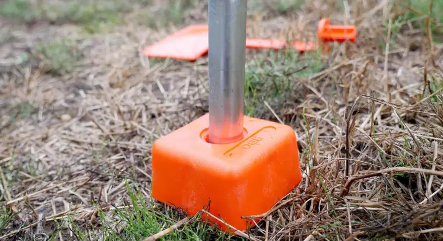 Borne orange avec un tube métallique planté dans le sol. D'autres bornes sont visibles en arrière-plan, indiquant le bornage d'un terrain déjà borné.