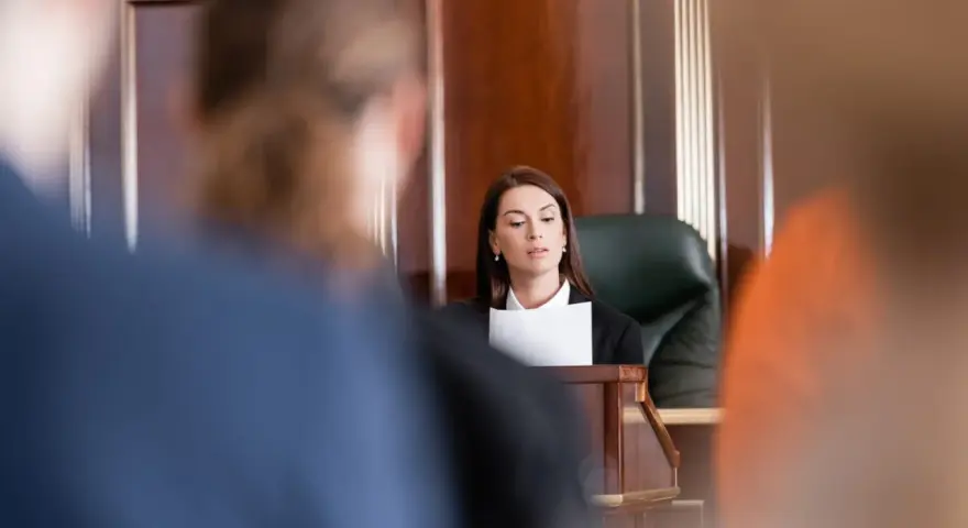 Une avocate présente son dossier, le dol, devant un juge. La salle d'audience est sombre et solennelle.