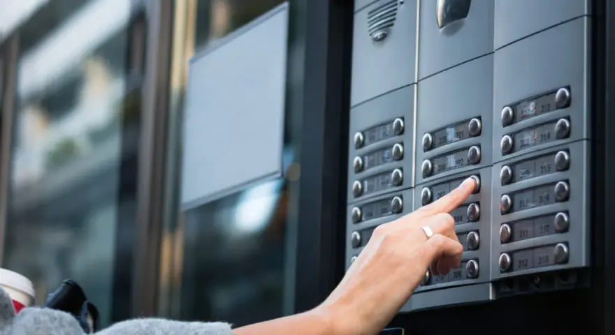 Une main appuie sur un bouton d'interphone, rappelant l'obligation du propriétaire d'assurer ce système.
