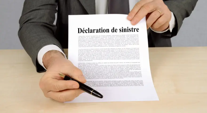 Un homme en costume gris tient un document intitulé "Déclaration de sinistre", prêt à signer.