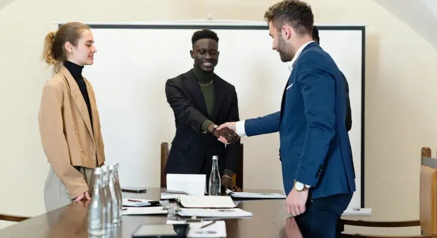 Trois personnes en tenue d'affaires se serrent la main. L'un d'eux discute des intérêts d'un compte séquestre notaire.