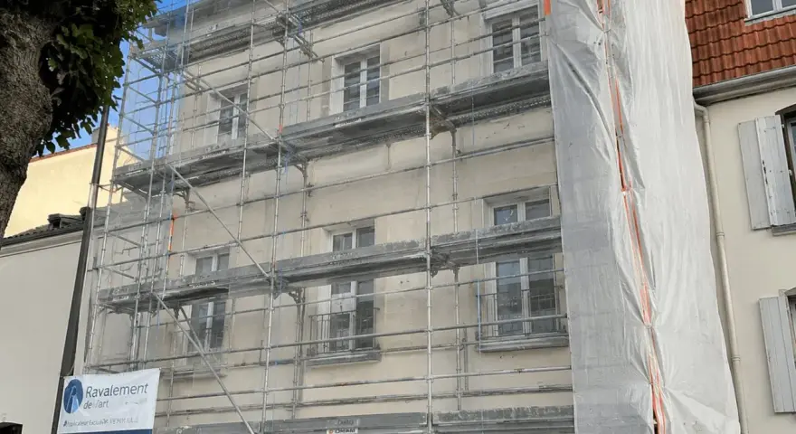 Ravalement de façade en cours, échafaudages recouvrant le bâtiment. Une bâche blanche protège une partie des travaux. L'indemnisation locataire est une préoccupation lors de ces rénovations.