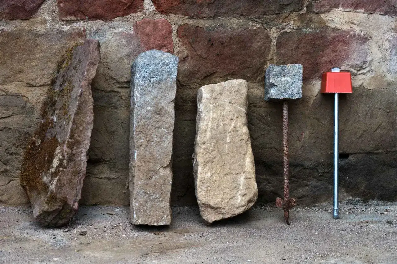 Quatre bornes, dont une borne cadastre ancienne, alignées devant un mur de pierres.