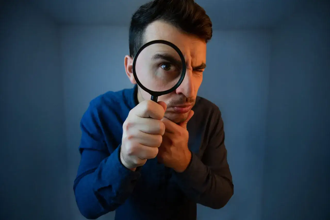 Homme examinant attentivement un contrat d'apporteur d'affaires immobili&egrave;res avec une loupe, l'air concentr&eacute;.