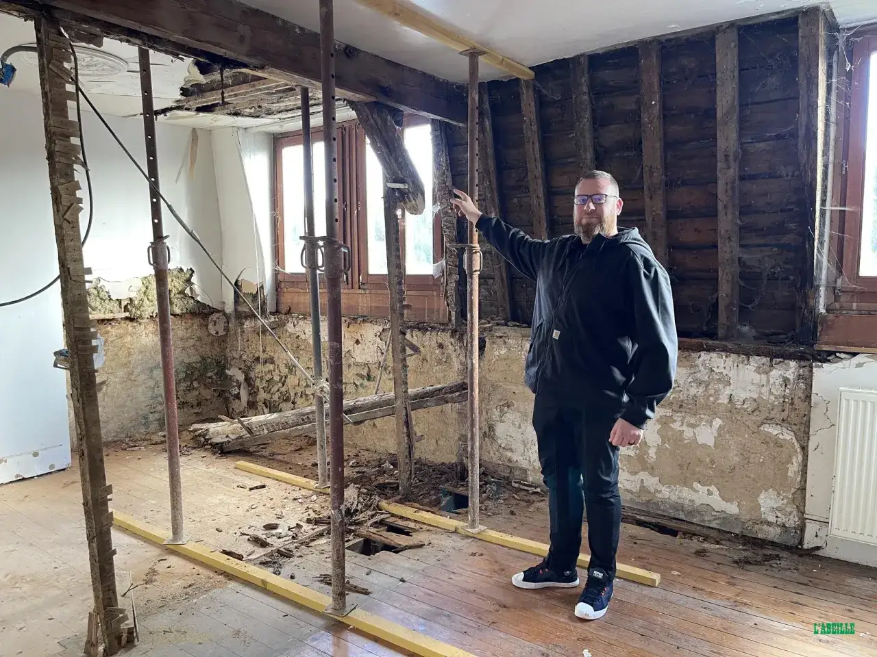 Un homme pointe du doigt une pièce en ruine, soutenue par des étais. La mérule a causé des dégâts importants, entraînant l'annulation de la vente.