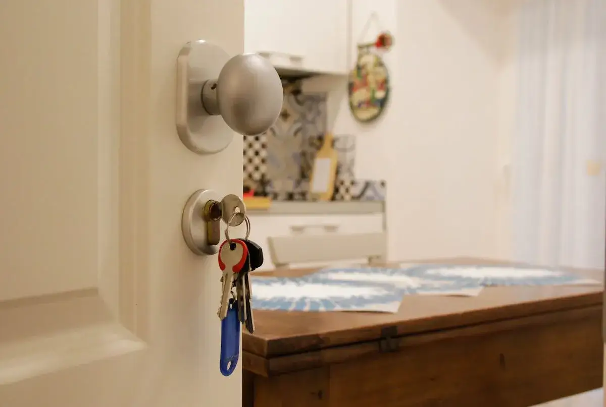 Clés dans la serrure d'une porte ouverte, symbolisant la reprise de bail d'un logement social. La cuisine est visible en arrière-plan.