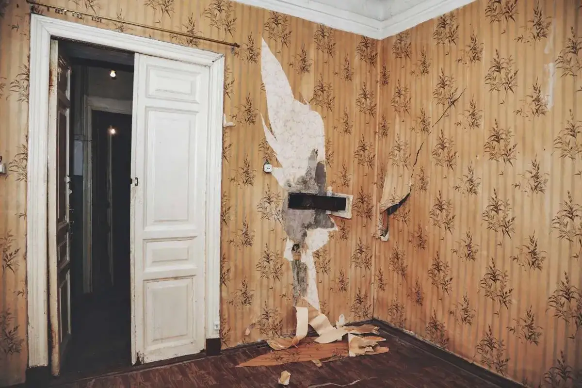 Intérieur délabré, papier peint déchiré et décollé, porte blanche abîmée. Vétusté après 10 ans de location.