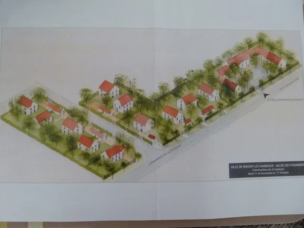 Vue aérienne d'un lotissement à Magny les Hameaux, avec des maisons aux toits rouges et des arbres. Le projet comprend 22 maisons.