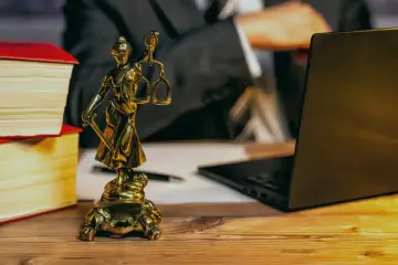 Statue de la justice, livres, ordinateur portable et stylo sur un bureau en bois. Un avocat examine les frais de donation.